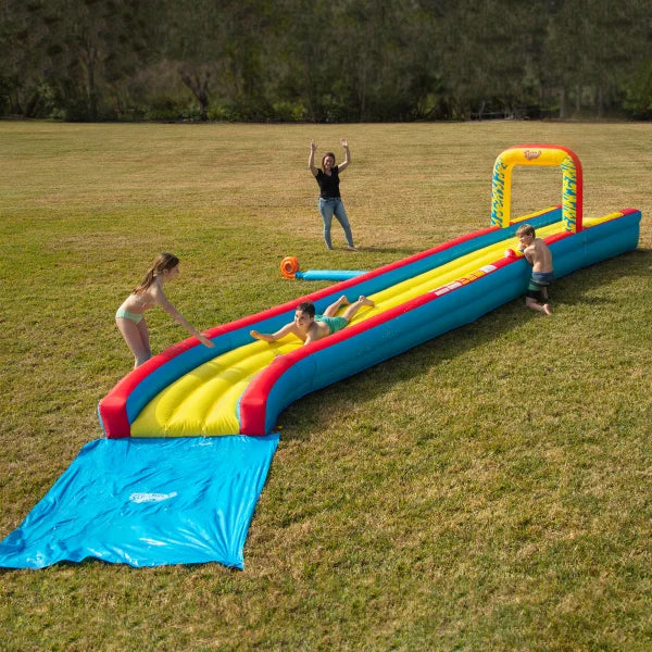 Children playing on an inflatable outdoor slip and slide water toy on grass with adult supervising