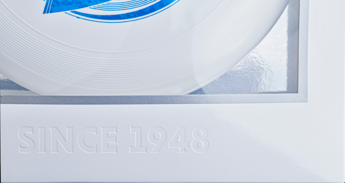 Close-up of commemorative Frisbee packaging showing white disc, blue detail, and 'Since 1948' text.
