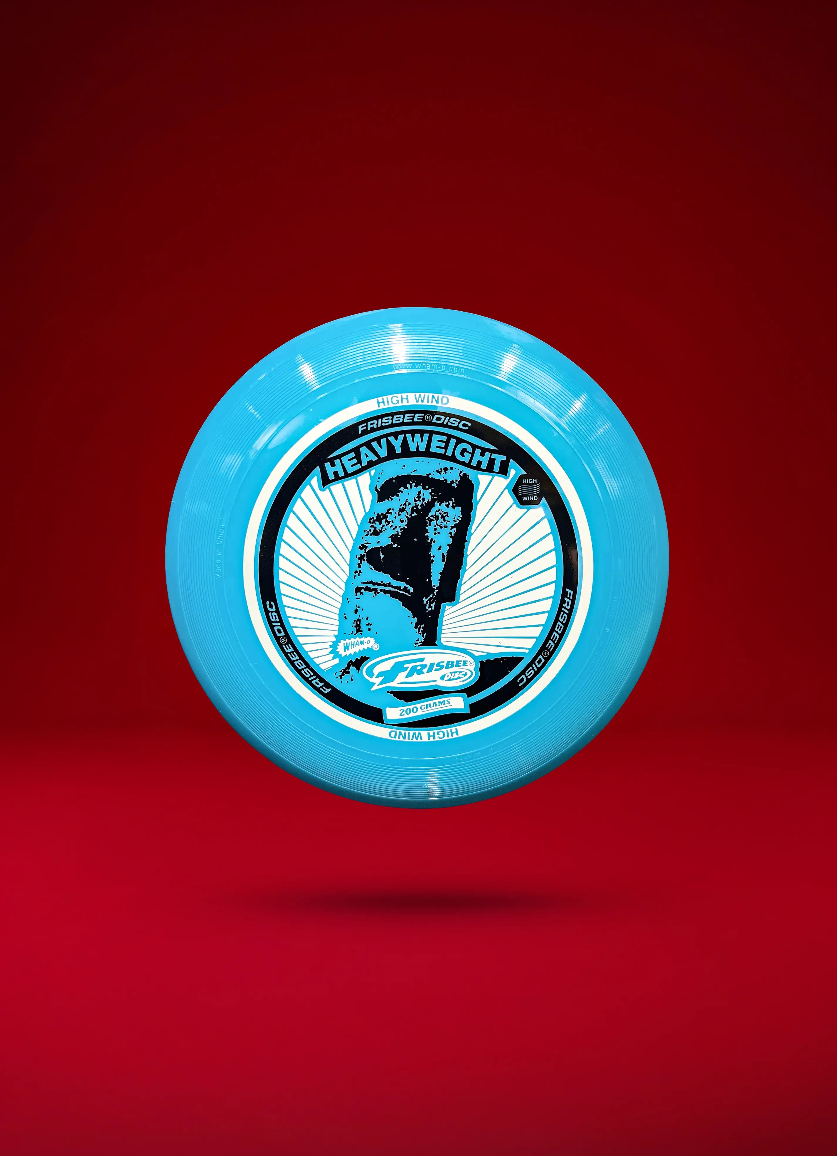 Blue heavyweight Frisbee disc with Moai graphic and high wind label on red background