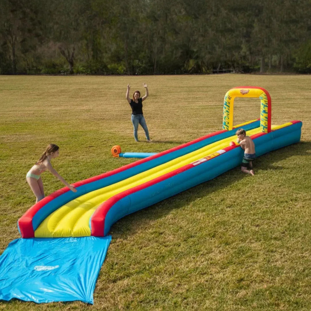 Kids playing on an inflatable slip and slide water toy in a large grassy yard.
