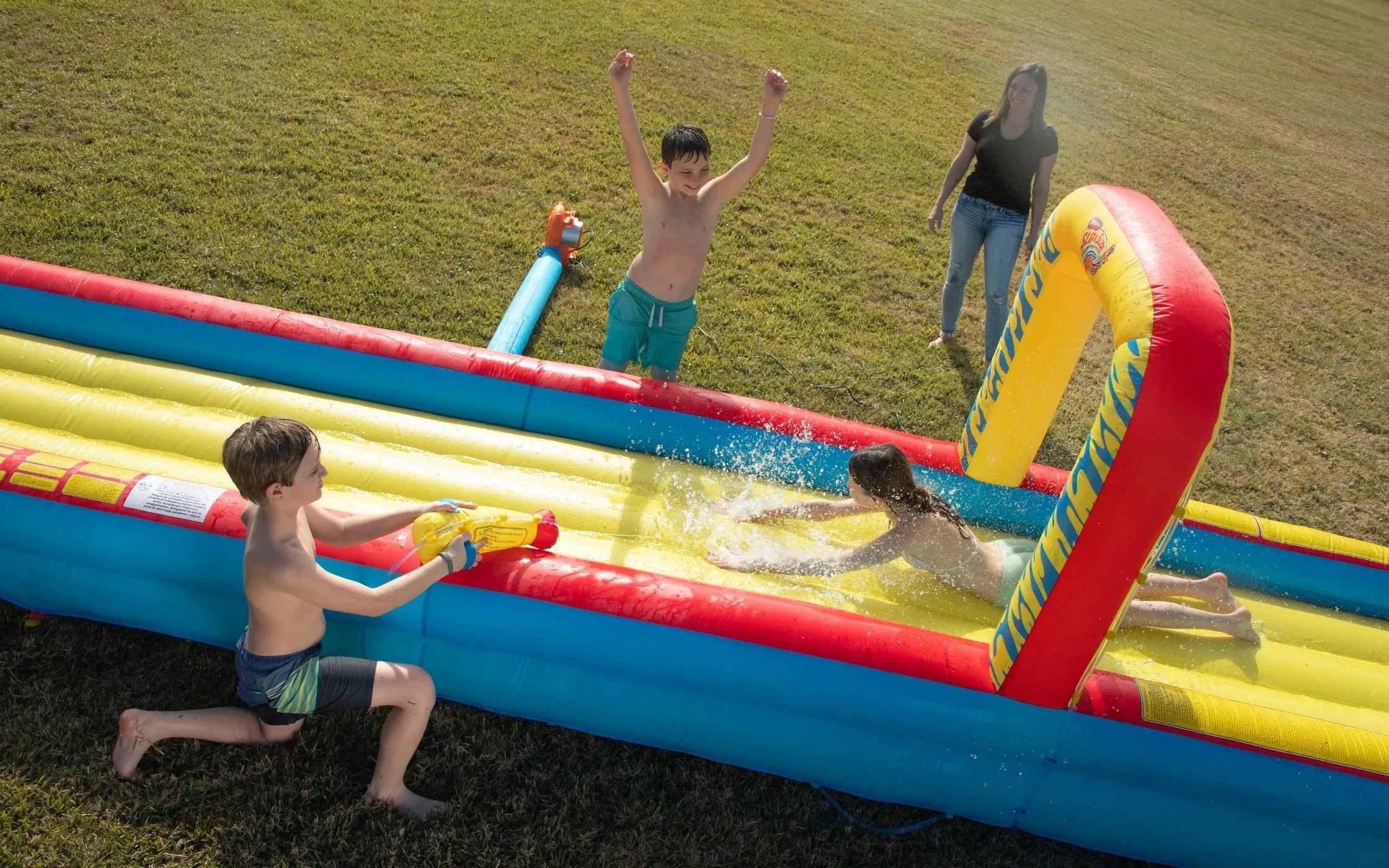 Kids playing on inflatable yellow and blue slip and slide water toy on grass in summer