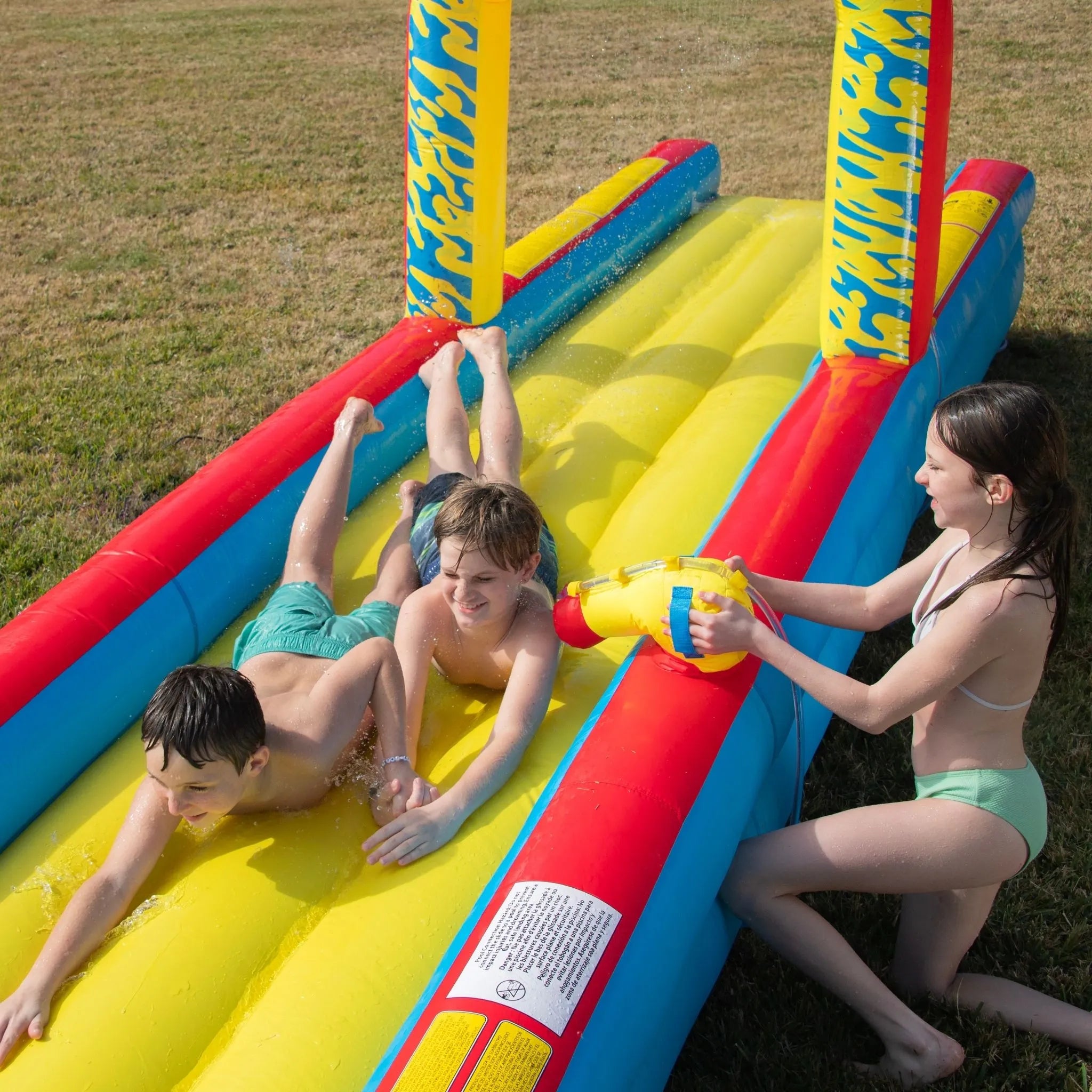 Kids playing on inflatable backyard water slide with bright colors and water sprayer.
