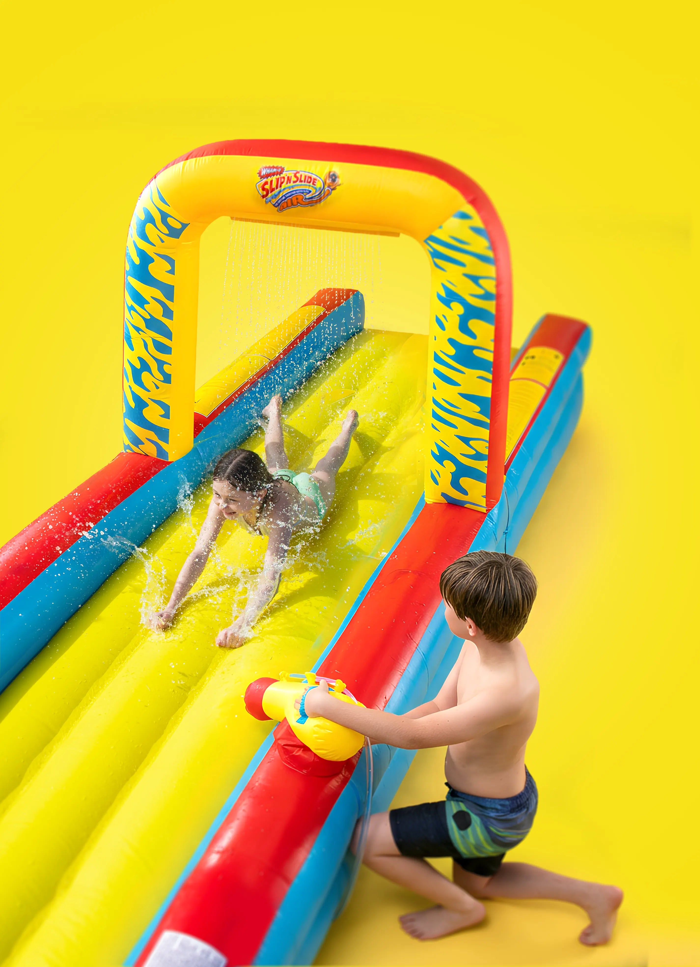 Two kids playing on inflatable Slip 'n Slide water toy with arch and bright yellow background.