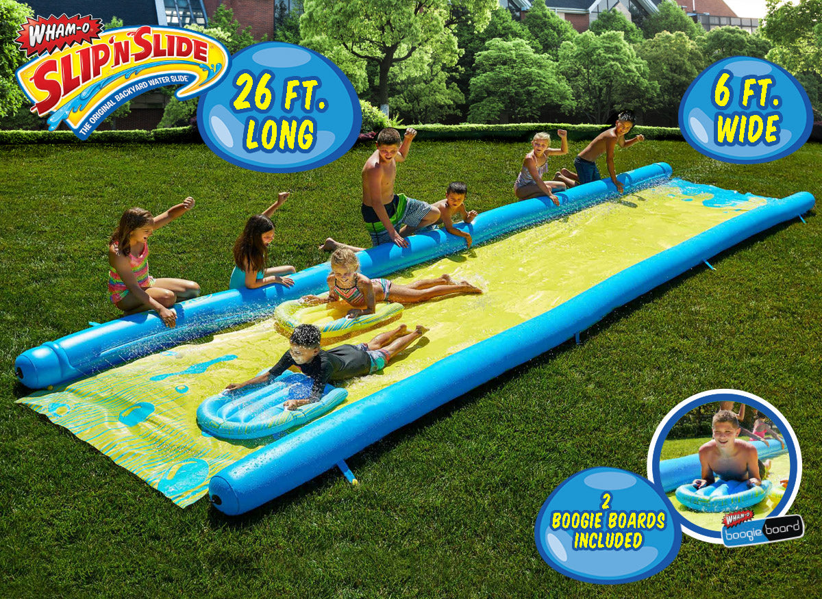 Kids playing on a 26 ft long Slip 'n Slide water slide with boogie boards in a grassy backyard.