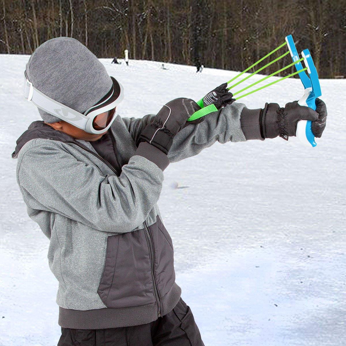 Child in winter gear using bright blue and green Wham-O snow slingshot outdoors in snow.
