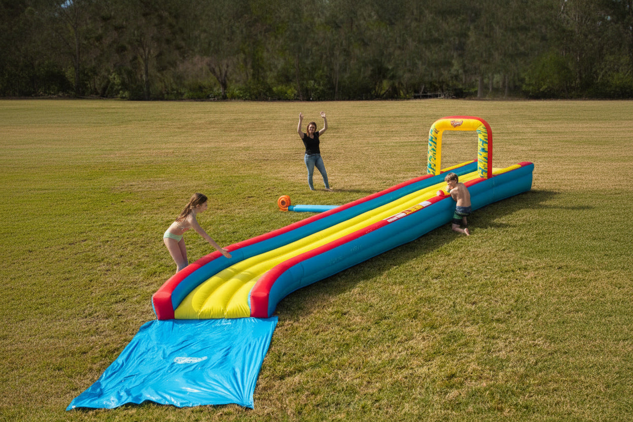 Kids playing on an inflatable backyard water slide on grass, having fun outdoors.