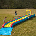 Kids playing on an inflatable slip and slide water toy in a large grassy yard.