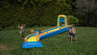 Kids playing on a colorful inflatable water slide on a green lawn in a sunny backyard