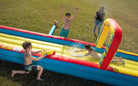 Children playing on a colorful inflatable water slide with water guns outdoors on grass