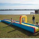 Children playing on inflatable water slip and slide in grassy backyard near lake on sunny day