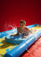 Smiling boy sliding on inflatable water slip and slide with splashing water, red background