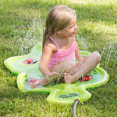 A girl is sitting on the Wham-O Giggle 'n Splash Lady Bug Sprinkle and Splash Play Mat 48"