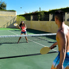 A man and a woman are playing Wham-O Game Time! Ultimate Paddle Ball in the Tennis court