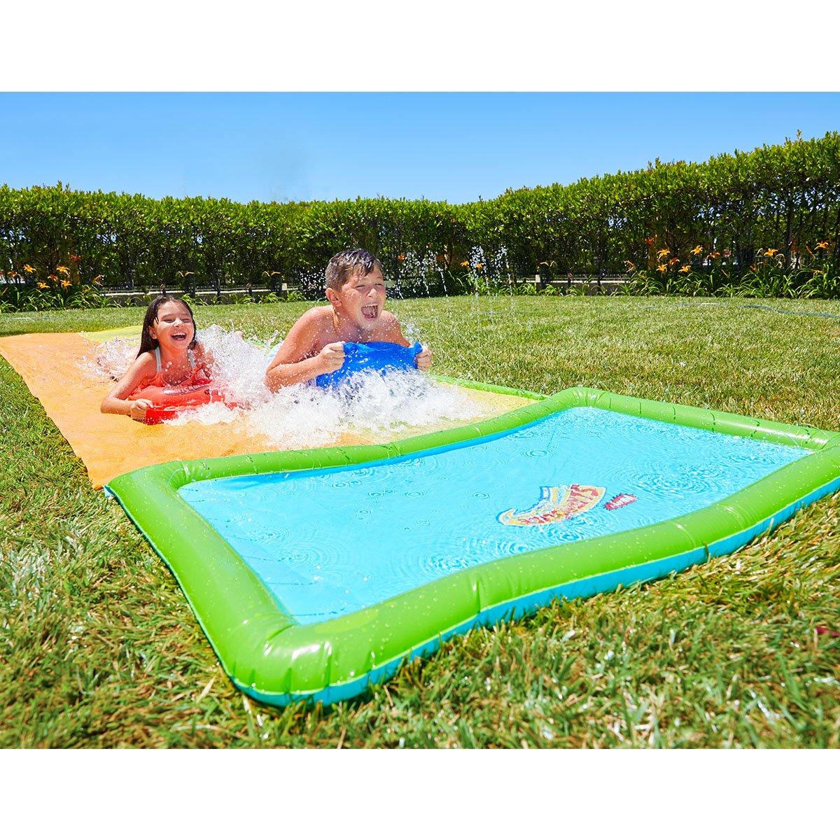 A boy and a girl is having fun with Wham-O Slip 'N Slide® Double Hydroplane XL in the backyard