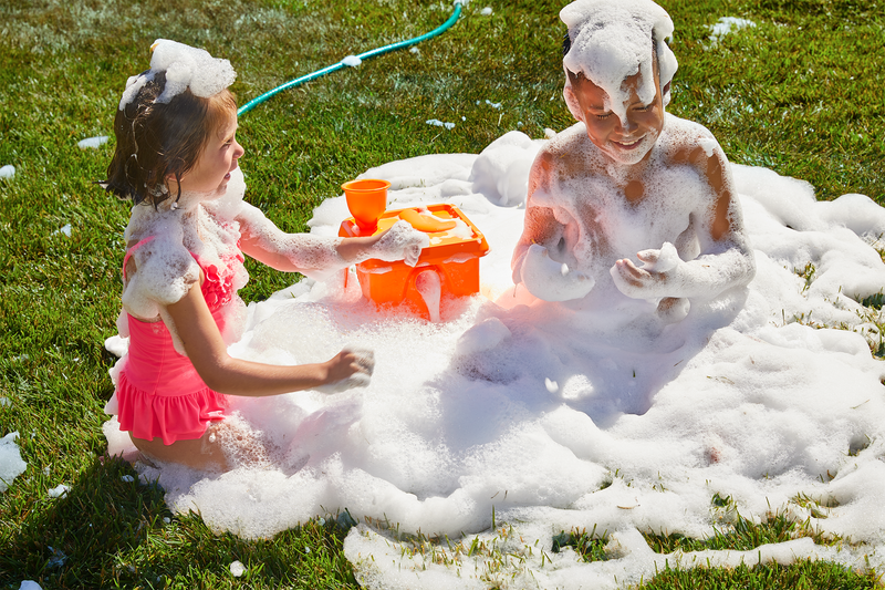 A boy and a girl is playing with Foam Party™ Foam Party Factory in that backyard